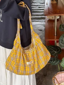 Detail shot of the yellow plaid tote bag showing texture, fabric folds, and sewn label craftsmanship.
