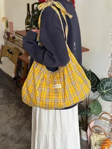 Close-up of yellow plaid pleated canvas tote bag, featuring detailed strap tie design.