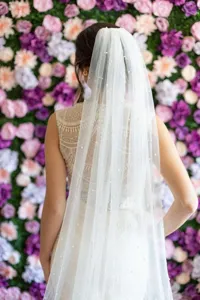 Detail view of a long bridal veil with delicate scattered pearls and comb, set against a floral wall.