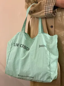 Light green canvas tote bag detail showing shoulder strap and printed English letters.