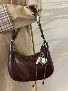 Nahaufnahme einer dunkelbraunen Lackleder-Achseltasche mit charmantem Mini-Baseball-Anhänger.