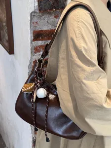 Nahaufnahme Detail der dunkelbraunen glänzenden Leder Achseltasche mit süßem Baseball-Anhänger.