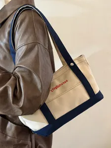 Λεπτομέρεια από την τσάντα tote canvas με λουρί ώμου και όμορφα κεντημένα γράμματα.