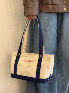Λεπτομέρεια από μια casual τσάντα tote από καμβά με μπλε χερούλια και κεντημένο κείμενο.