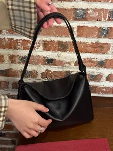 Black minimalist soft leather underarm bag detail view showing fine texture and sleek design.