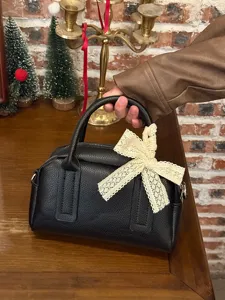 Black Boston handbag detail shot featuring a delicate lace bow and leather texture.