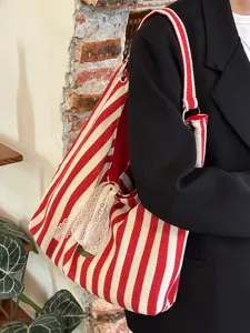 Close-up detail of red white striped canvas shoulder bag featuring a cute lace bow pendant.