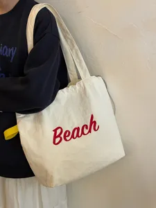 Detailansicht einer lässigen, weißen Segeltuchtasche mit rotem Buchstaben-Print und Henkel.