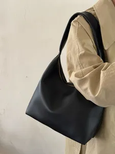 Detail view of a minimalist black soft leather shoulder underarm bag worn by a model.