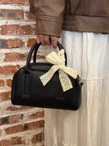 Detail view of black leather Boston handbag featuring an elegant beige lace bow handle accent.