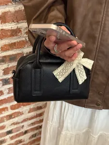 Close-up of black leather Boston handbag featuring a delicate beige lace bow detail.