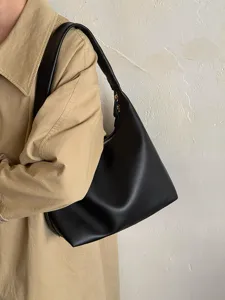 Detailed view of minimalist black soft leather underarm shoulder bag worn with trench coat.