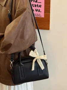Detailed view of the black Boston handbag featuring a cute beige lace bow accent and leather strap.