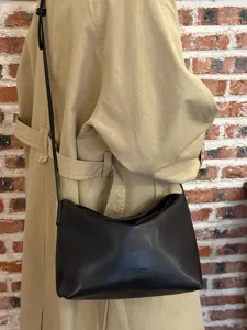 Detailed view of minimalist black soft leather underarm shoulder bag worn against brick wall.