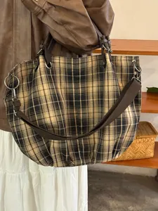 Detailansicht der karierten Canvas-Umhängetasche, lässiges Design mit braunen Trägern.