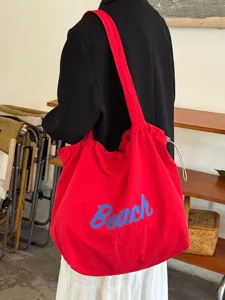 Detailansicht einer roten Canvas-Schultertasche mit blauem Beach-Buchstaben-Print.
