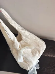 Detailed close-up view of elegant cream white lace floral shoulder tote bag with bow detail.