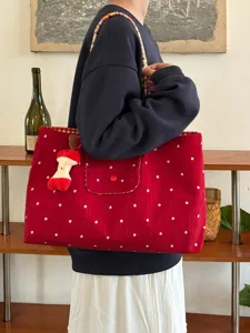 Red canvas tote bag detail, featuring floral print, woven strap and cute plush apple charm.
