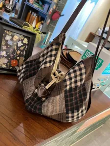 Close-up detail of retro plaid canvas shoulder bag, showing vintage patchwork texture.