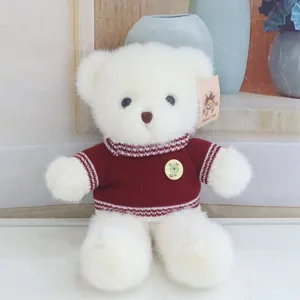 Cute white teddy bear plush toy wearing a warm maroon knitted sweater, detailed shot.