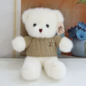 Cute white plush teddy bear wearing a cozy brown knit sweater with a metal bee brooch.