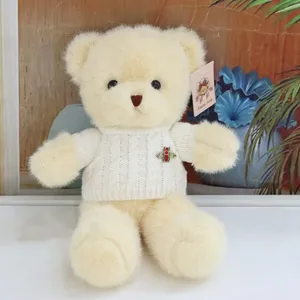 Beige teddy bear plush toy wearing a white knit sweater with a cute bee brooch detail.