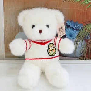 Cute white teddy bear plush toy wearing knit sweater with red trim and cute crest badge.
