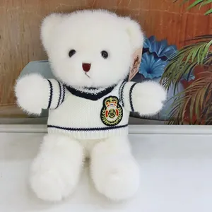 Close-up detail of white plush teddy bear wearing striped sweater and crest embroidery.