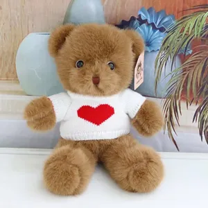 Cute brown plush teddy bear toy wearing a white knitted sweater with red heart for kids.