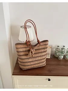 Detail view of woven straw tote bag with brown leather straps and tassels, casual beach style.
