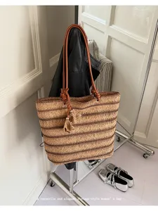 Close-up detail of the woven straw tote bag with brown leather handles and chic tassel charm.