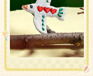 Close up shot of cute embroidered bird patch with red hearts on tree branch detail view.