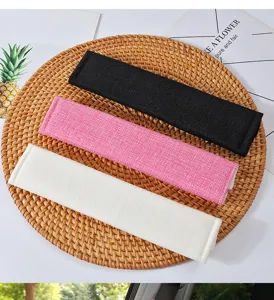 Close-up of linen car seat belt shoulder covers in black, pink, and white on woven mat.
