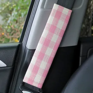Pink and white plaid car seatbelt shoulder pad installed in vehicle interior for comfort.