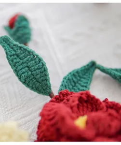 Détail de fleur de camélia crochetée à la main, superbes pétales en laine rouge et feuilles vertes.