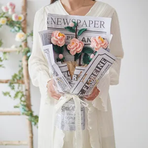 Handgefertigter Häkel-Kamelien-Blumenstrauß, eingewickelt in Zeitungspapier für Geschenke