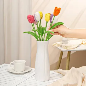 Close-up detail of handmade crochet tulip flowers bouquet in a white ceramic vase, home decor.