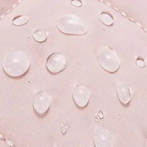 Waterproof quilted fabric detail of women's shoulder bag, showing soft pink texture and water drops.