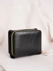 Close-up detail of women black trifold wallet with gold zipper and smooth texture.