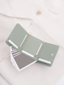 Close-up detail of a sage green trifold wallet with multiple card slots and snap closure.