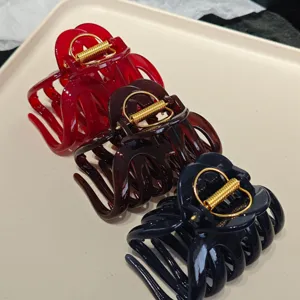 Close-up detail of three large resin hair claw clips in red, brown, and black with metal springs.