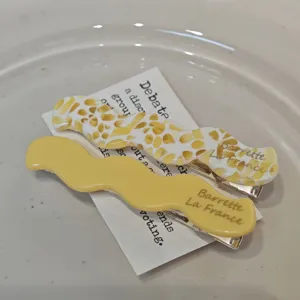 Detail view of two retro acetate wavy hair clips in solid yellow and patterned designs.