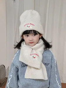 Detail shot of cozy children knitted hat and scarf set with cute bear embroidery, soft winter warm.