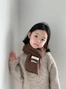 Detailed close-up of soft brown knitted children winter warm scarf with cloth label.