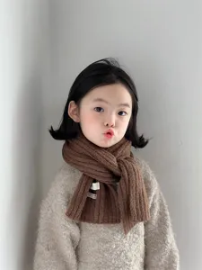 Detailed view of kids knit scarf in brown wool with fabric label, soft winter warm accessory.