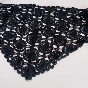 Detailed close-up of a black crochet lace triangular scarf showing exquisite floral pattern texture.