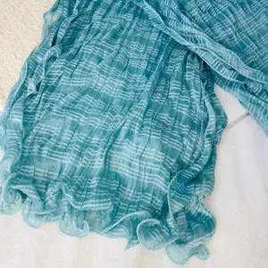 Close-up detail view of blue-green pleated textured gauze scarf fabric and soft drape.