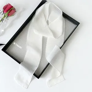 Detail view of a solid white long ribbon scarf, elegant hair band and chic bag accessory.