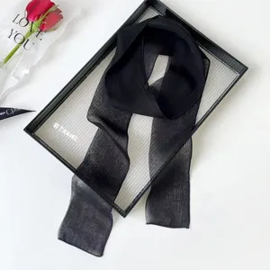 Black sheer long scarf detail shot, elegant thin ribbon accessory displayed on a chic tray.