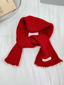 Detailed view of red knitted kids scarf with white scalloped edge and woven brand label.